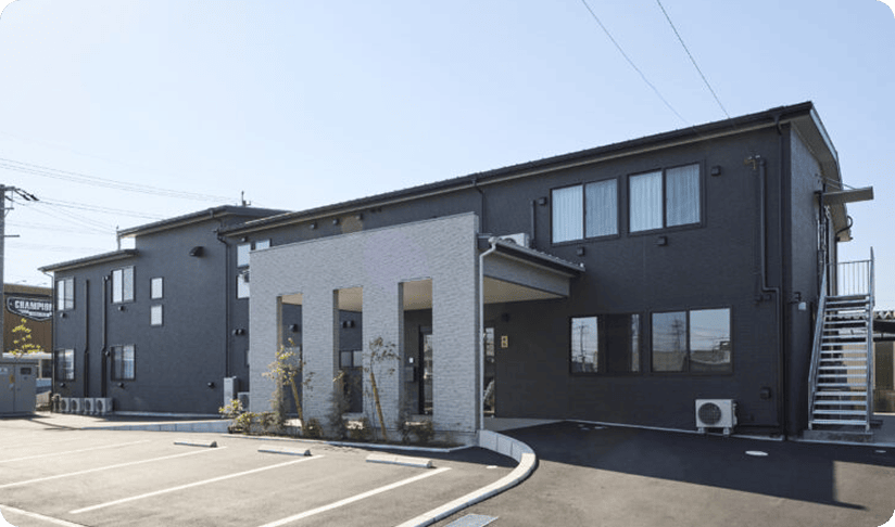 駐車場が広がる二階建て建物の外観（晴天）